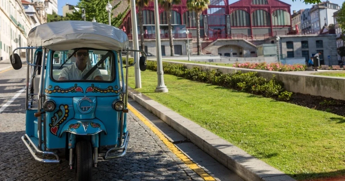 Blue decorated tuk-tuk on a street beside a park and a market building