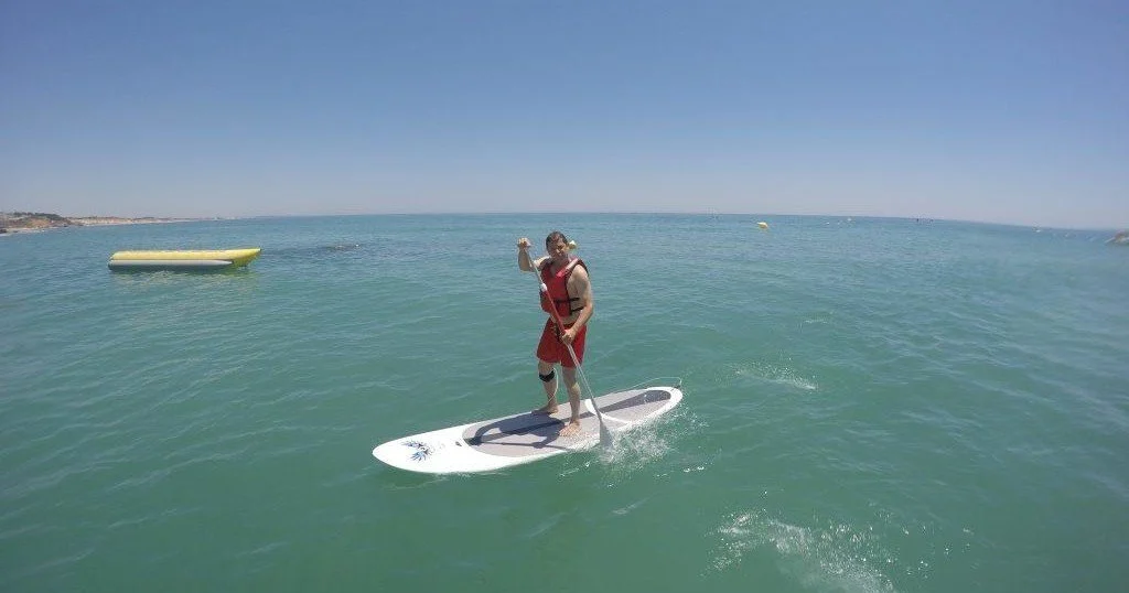 SUP’er in rood shirt op rustig groen water met een drijvend platform op de achtergrond