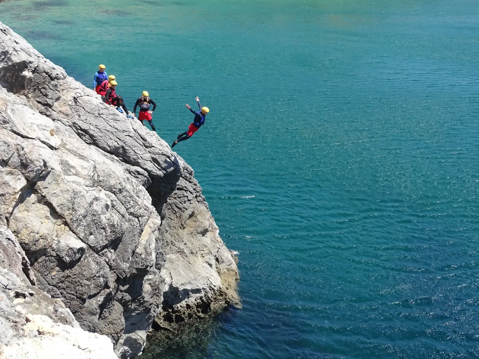 People jumping from a rock ledge into turquoise water