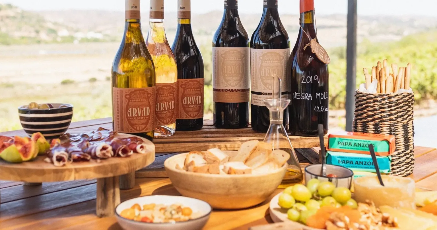Wine bottles and a charcuterie spread on a table above vineyards