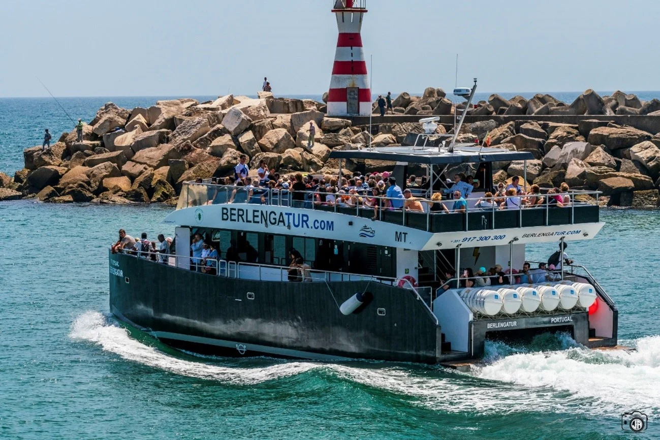 Catamaran ferry full of passengers leaving a harbour with a striped lighthouse