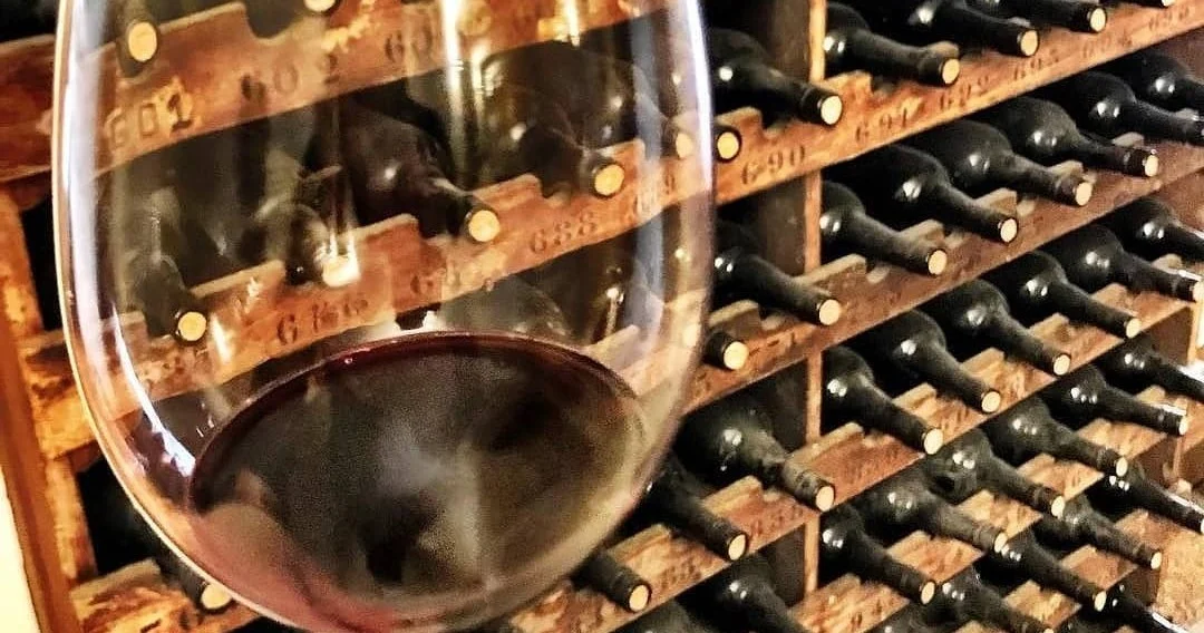 Glass of red wine in front of racks of bottles