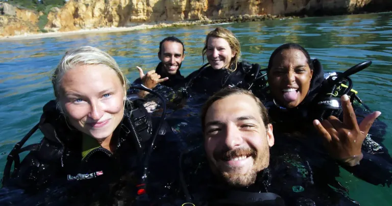 Group of smiling divers in wetsuits taking a selfie in the water