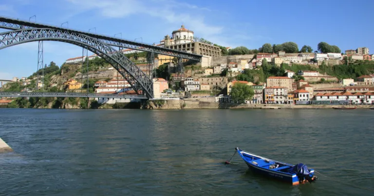 Small blue boat on the river below an iron arch bridge and a hillside city