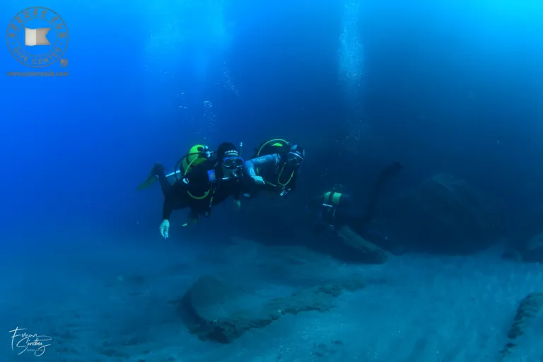 Divers over a sandy seabed in deep blue water