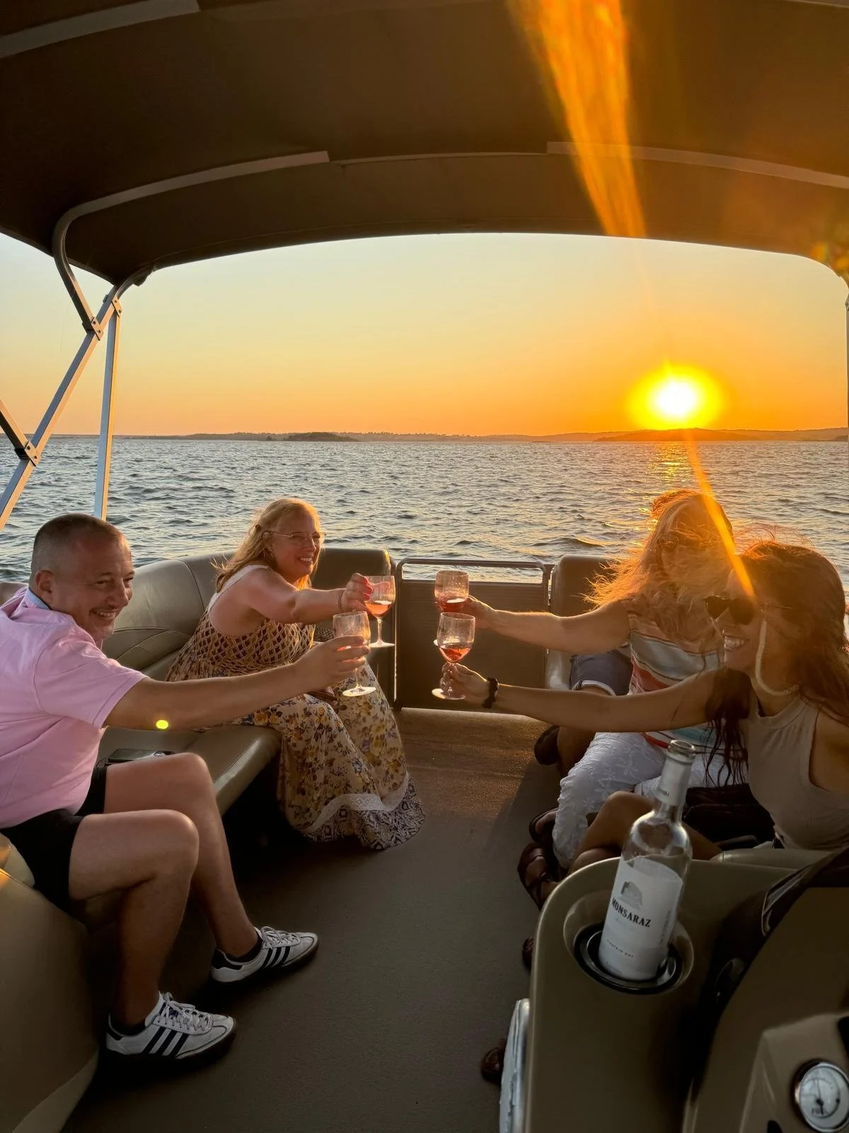Guests raising glasses on a covered boat as the sun sets over the water