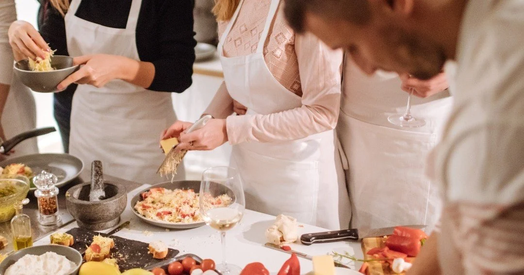 Chef and guests preparing dishes together at a long table
