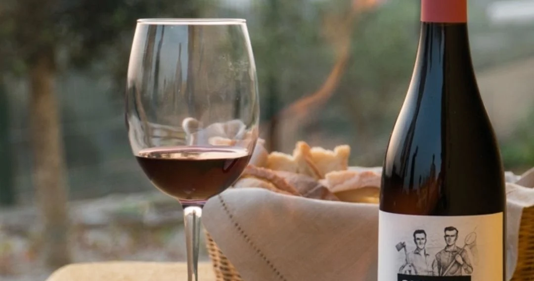 Copa de vino tinto junto a una botella y una cesta de pan