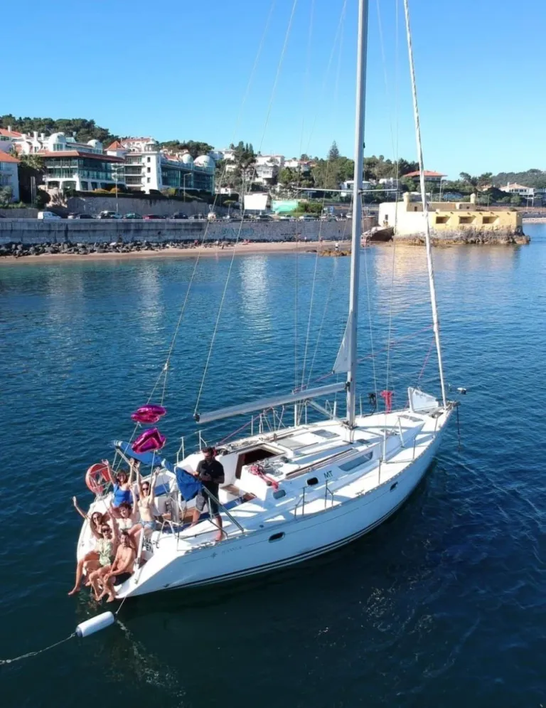 White sailboat with guests aboard on calm water near a beach town