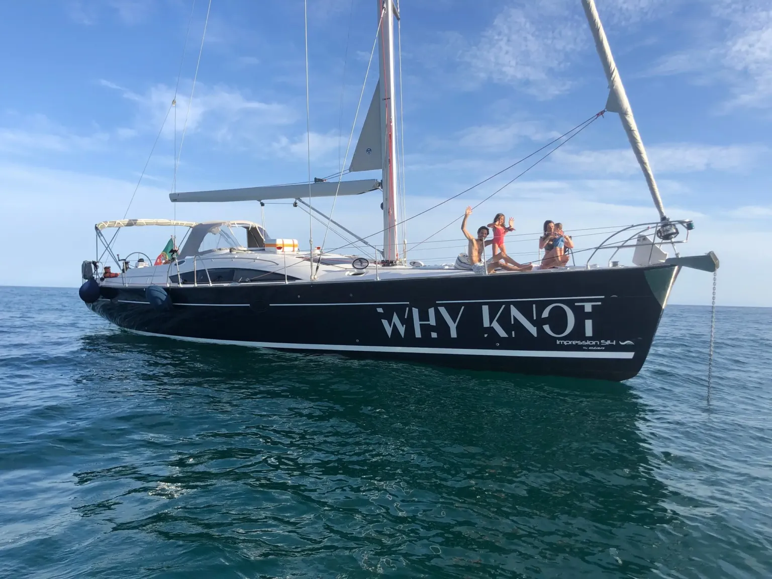 Black-hulled sailing yacht named Why Knot with guests on deck