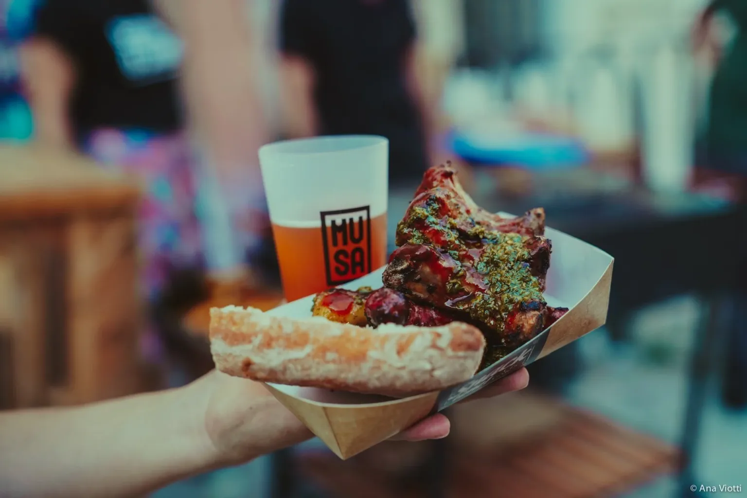 Hand holding a tray with a pizza slice and a cup of beer