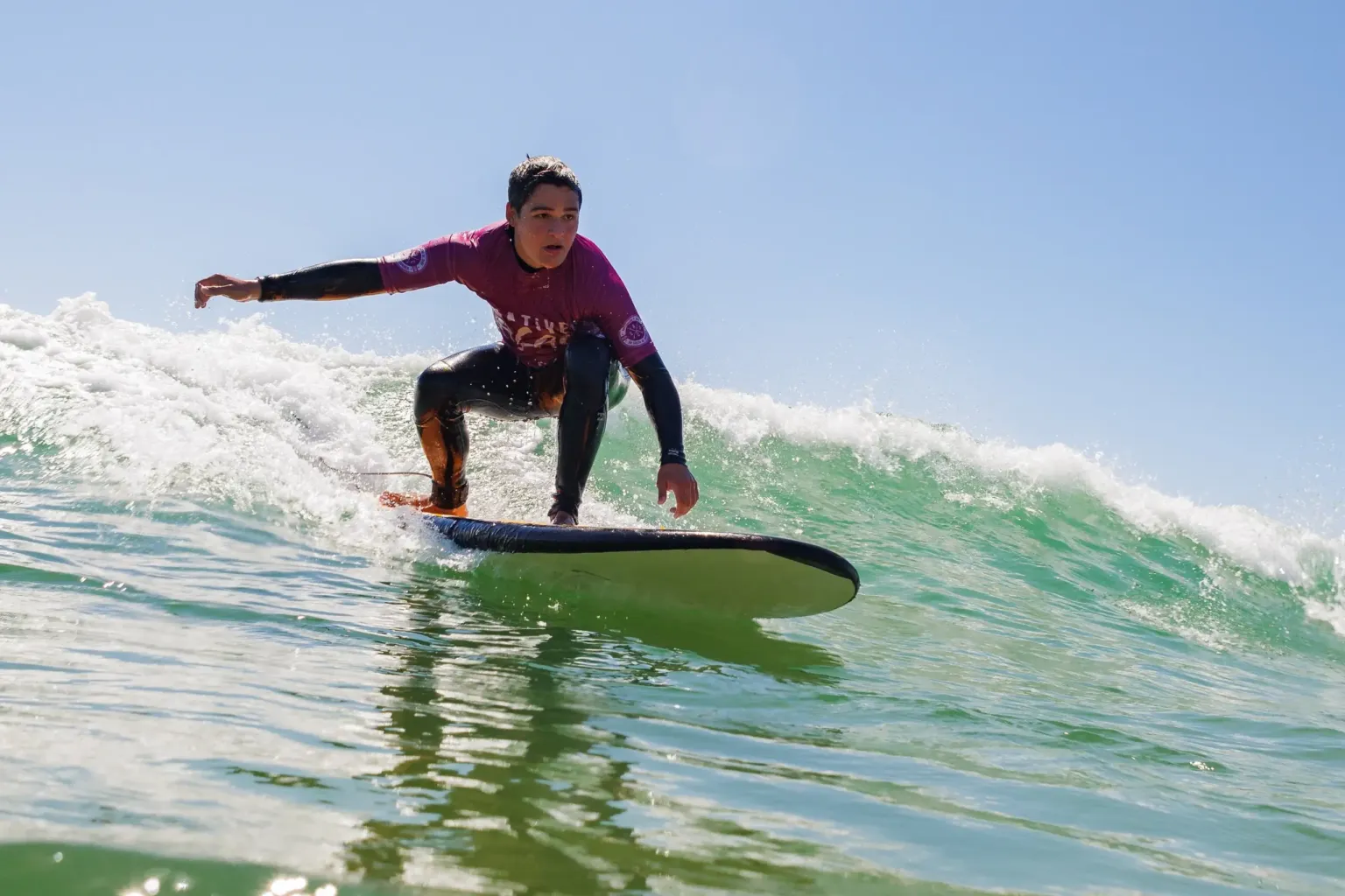Surfer in a burgundy wetsuit riding a small green wave