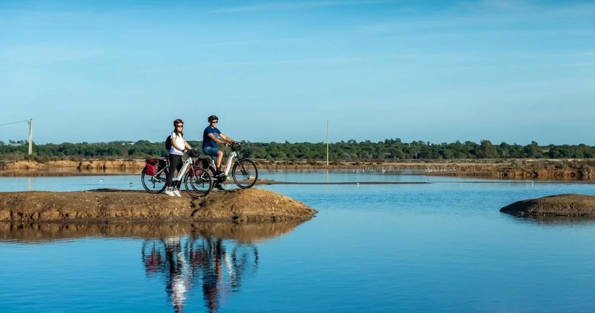 Dwóch rowerzystów jedzie wąską groblą między lagunami i salinami
