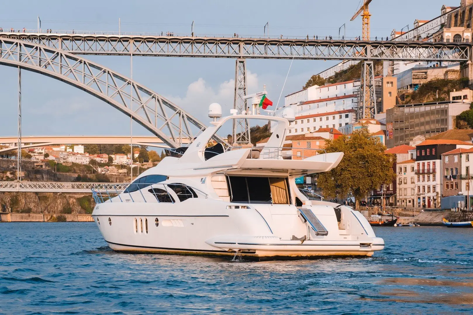 White yacht on the river in front of an iron arch bridge